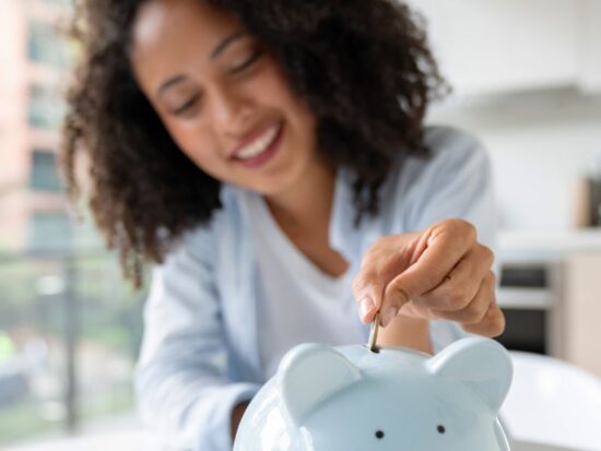 Pieniądze szczęścia nie dają? Na zdjęciu kobieta wrzuca monety do skarbonki.